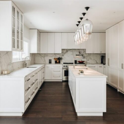 Luxury white kitchen with marble countertops and backsplash, island sink, shaker cabinets, dark wood flooring, glass pendant lights, and high-end residential interior design.